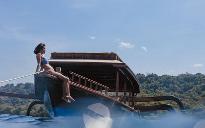 安缦湾澜度假村中，一艘传统木制船只停泊在碧蓝海水旁，船上放置着棕色帆布遮阳篷。