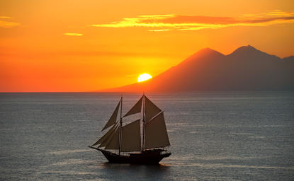 Sailing vessel anchored at Amandira as the sun sets over the ocean and distant mountains.