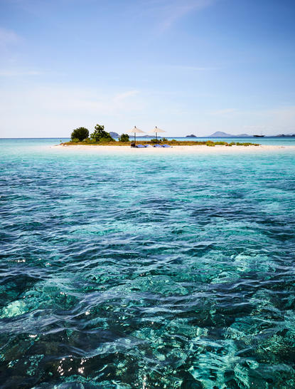 Amandira's island emerges from turquoise waters beneath clear skies, Indonesia.
