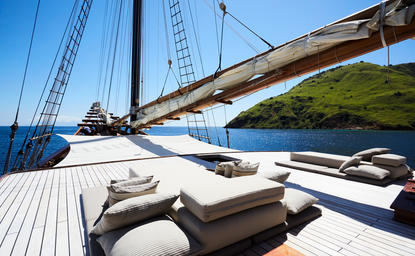 Sun deck loungers on sailing yacht moored at Amandira, with clear blue waters and coastline visible beyond.
