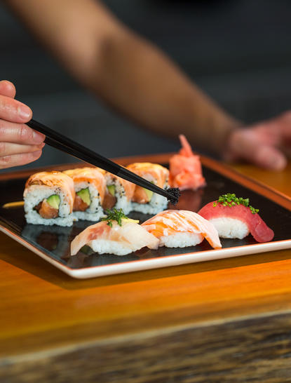 Hand reaching towards a plate of assorted sushi at Amanpulo.