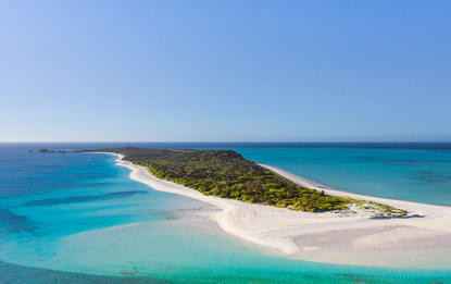 Aerial view of Amanpulo's white sand beach and turquoise waters meeting a forested island.