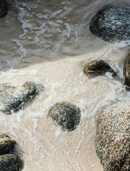 Shallow waves washing over sand and dark rocks at Amanpuri resort.