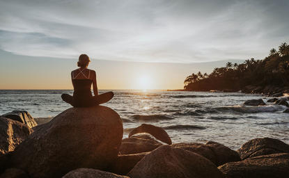Person meditating on rocks at sunset, Amanpuri resort, Thailand.