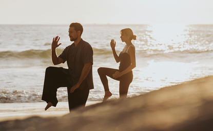 Three people practising yoga on Amanpuri's beach at sunrise.