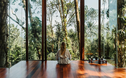 Amanpuri wellness overview: open-sided pavilion with wooden flooring overlooking forested landscape through tall windows.