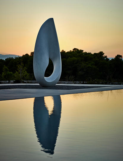 Sculpture blanche se reflétant dans un bassin au coucher du soleil à la station Amanzoe.