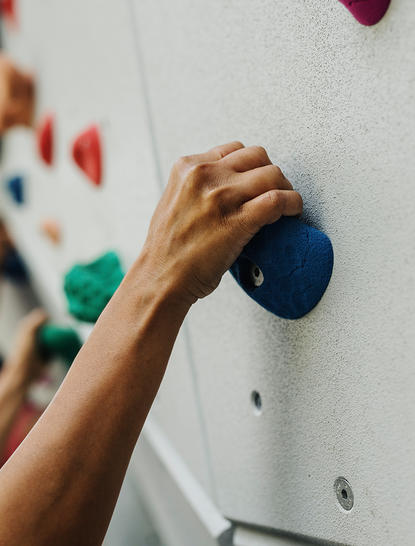 Climber's hand reaching for a blue hold on the climbing wall at Amanpuri resort.
