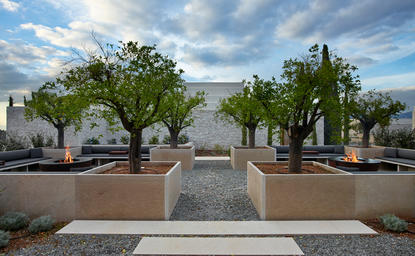 Dining villa at Amanzoe resort with symmetrical gardens and Mediterranean architecture beneath blue sky.