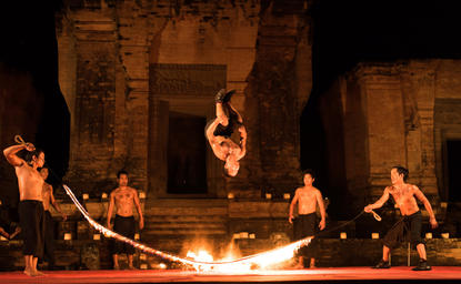 Candlelit private dinner setting at Amansara with guests seated around an open flame on a terracotta stage.