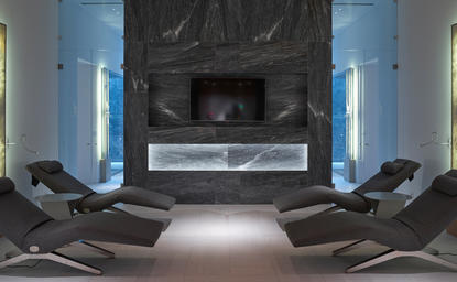 Spa relaxation area at Amanzoe resort with symmetrical black loungers facing a central fireplace.