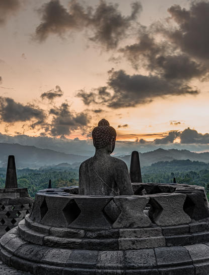 Silhouette d'une personne assise face aux volcans au coucher du soleil à Amanjiwo, resort en Indonésie.