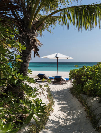 Pathway through beach vegetation leading to sandy shore and umbrella at Amanpulo resort.