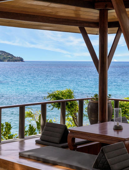 Deluxe Ocean Pavilion at Amanpuri with wooden beams framing turquoise sea views, potted plants and workspace.