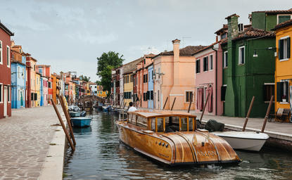 Wooden boat moored on a Venice canal with colourful buildings lining the waterway at Aman Venice.