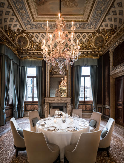 Ornate dining room at Aman Venice with crystal chandelier above round table set for dining.