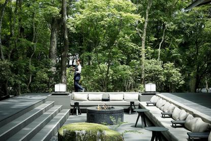 アマン京都のリゾートにある、緑に囲まれたテラス席。木製デッキの上に配置された現代的な家具と植栽。