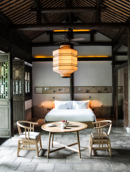 Village Suite at Amanfayun with circular dining table, woven chairs, and pendant lighting beneath exposed timber beams.