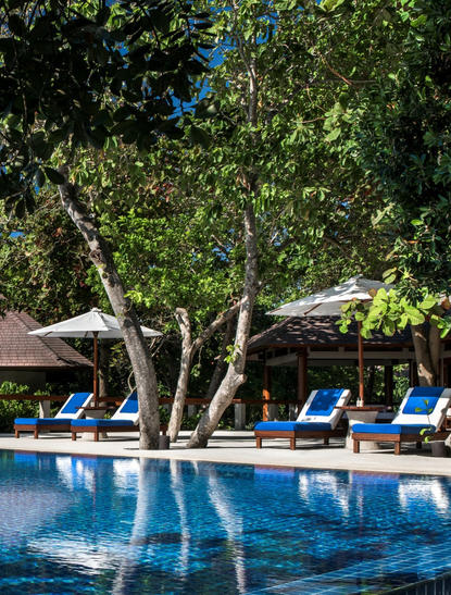 安缦璞乐度假村的四卧别墅，泳池畔有蓝色躺椅和大树。