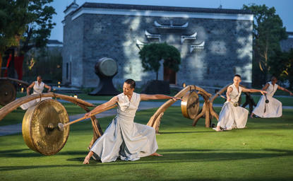 Performers in period costume on grass during U Theatre performance at Amanyangyun, with traditional building backdrop.