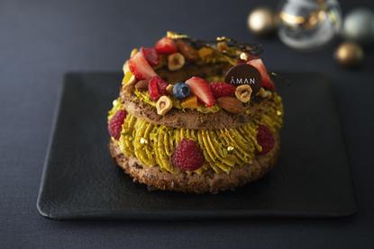 Aman Tokyo Christmas cake with gold leaf and red berry garnish on black plate.