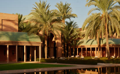 Amanpulo resort courtyard with palm trees and terracotta-coloured buildings reflected in still water.