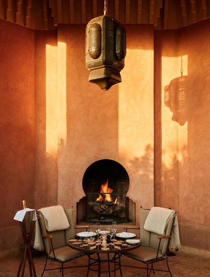 Al Hamra Maison fireplace with two chairs and warm terracotta walls at Amanjena.