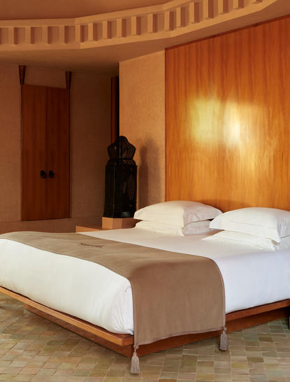 アマンジェナ リゾートのパビリオン宿泊施設の寝室。ウッドパネルの壁と温かみのある照明が特徴。