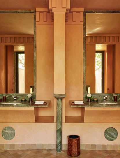 Symmetrical pavilion bathroom at Amanjena with twin mirrors, terracotta columns, and warm stone walls.
