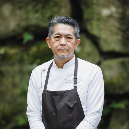 Hiroyuki Matsuo, Executive Pastry Chef at Aman Kyoto resort, wearing a white chef's shirt and dark apron against a blurred garden background.