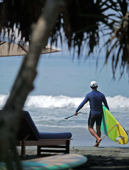 Paddleboarder in wetsuit heading towards the sea at Amankila's beach club, Indonesia.