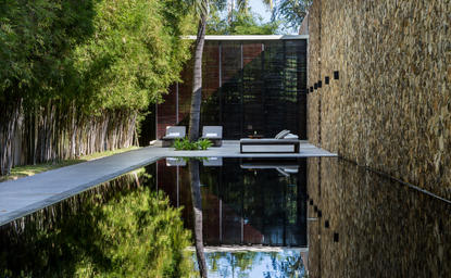 Reflecting pool at Amansara with tree-lined pathway and traditional architecture.
