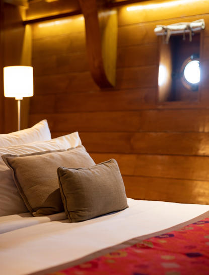 Deluxe cabin bedroom at Amandira with wooden walls, bed with cushions and red throw, and ambient lighting.