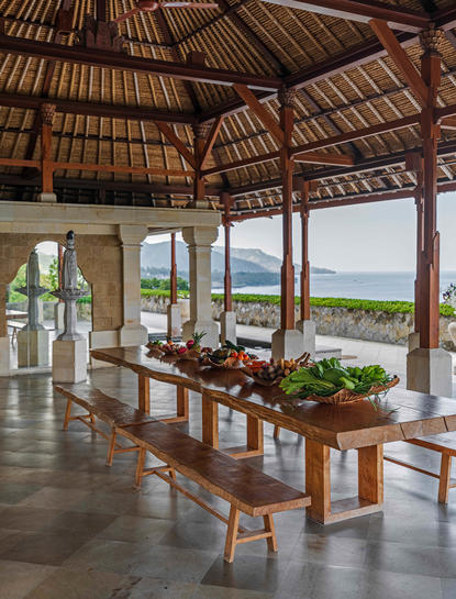 Harvest table at Amankila resort with ocean views and wooden pavilion architecture.