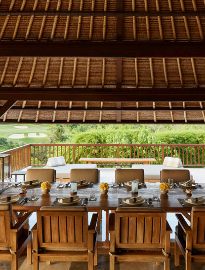 Dining pavilion at Aman Villas at Nusa Dua with wooden table, chairs, and soaring timber ceiling opening to tropical gardens.