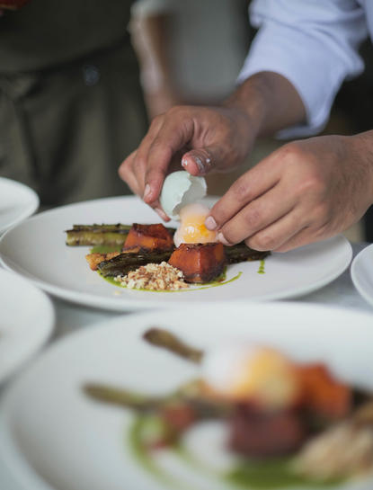 Hands plating a colourful dish at Amanjiwo resort's dining venue, Indonesia.