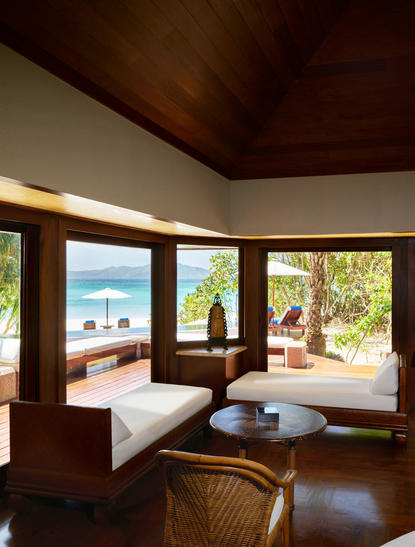 Amanpulo beach pool casita living room with wooden ceiling, daybed, and views to tropical garden and sea.
