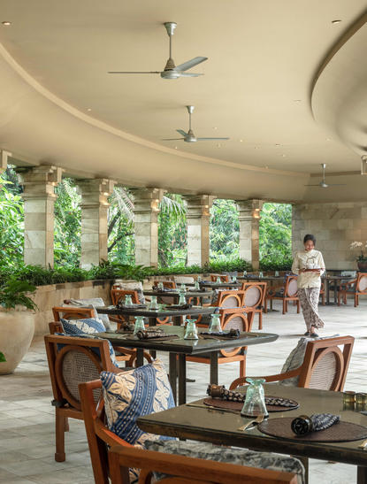 Pool Club at Amanjiwo, with wooden dining chairs and tables beneath curved ceiling and verdant views.