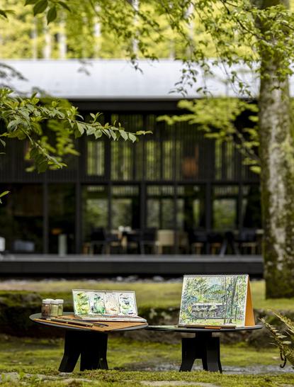 安缦京都度假村内的日式花园，两张木制长椅面向绿色植被和传统建筑。