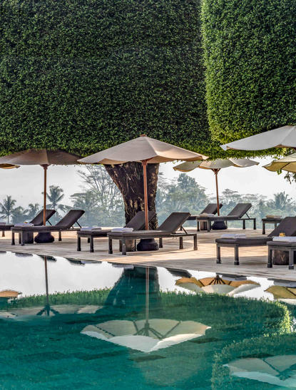 Poolside seating area at Amanjiwo with sunloungers, umbrellas and lush green hedging.