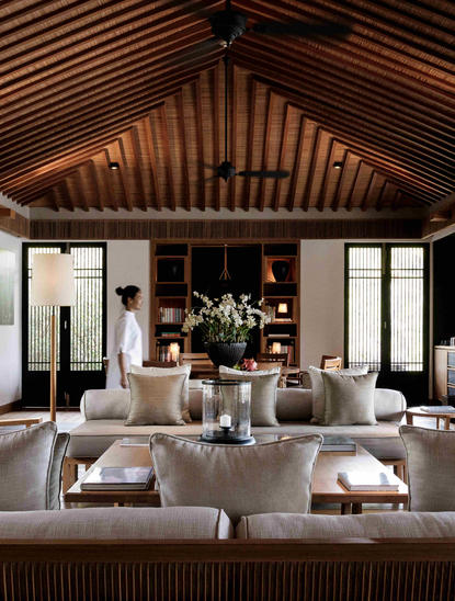 Lounge dalam residence di Amanoi dengan ceiling kayu bergaris, sofa netral, dan pencahayaan hangat.