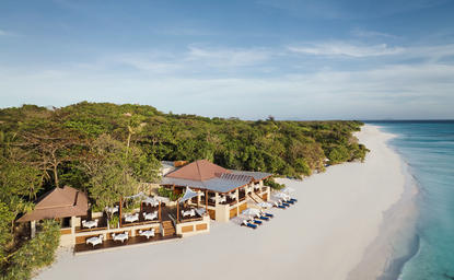 Aerial view of a beachfront dining venue at Amanpulo with thatched structures along white sand and turquoise waters, Philippines.