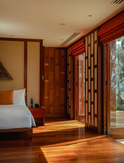 Amanpuri resort principal bedroom with wooden screens, warm timber flooring and natural light from the garden.