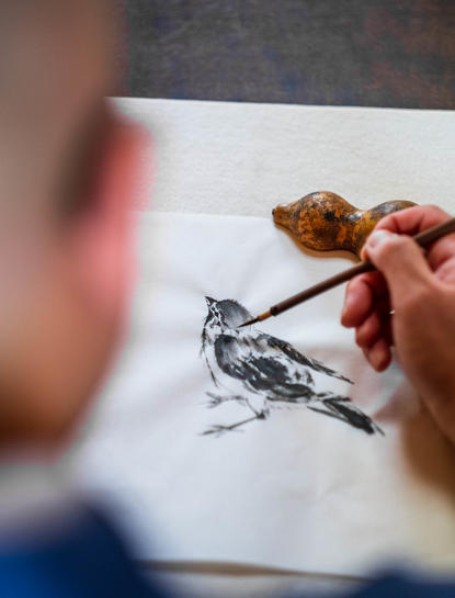 安缦京都度假村内，艺术家用毛笔在纸上绘制水墨画中的鸟类。