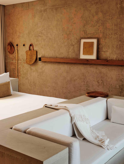 Amangiri principal bedroom with terracotta walls, wooden beam and minimal furnishings.
