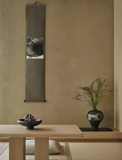 Pavilion room at Aman Kyoto resort with minimalist décor, featuring a tall wooden panel, ceramic vessels, and a single plant stem.
