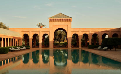 Central basin at Amanjena, a symmetrical courtyard with arched colonnade reflected in still water at sunset.