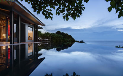 Exterior pool at Amanoi resort overlooking calm waters at dusk, with forested headland beyond.