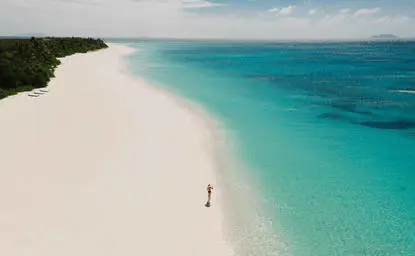 Amanpulo's sandy beach stretches along turquoise waters, with a solitary figure standing on the white sand.