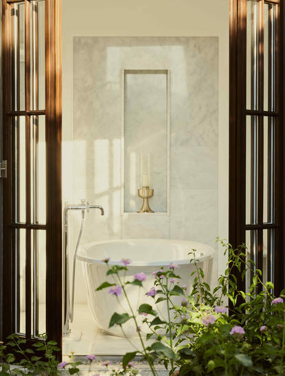 Marble bathroom entrance at Amanruya with garden views through open black-framed doors and potted greenery.